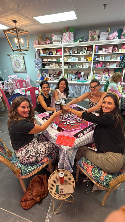 Group of women sitting around a table in a store, raising their hands in a celebratory manner.